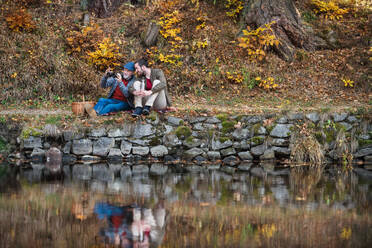 Älterer Vater und sein Sohn mit Fernglas und Picknickkorb sitzen am See in der Natur. - HPIF26708