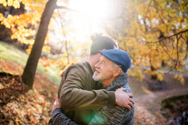 Ein älterer Vater und sein Sohn beim Spaziergang in der Natur, die sich bei Sonnenuntergang umarmen. - HPIF26713