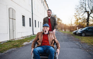 Ein junger Mann und sein älterer Vater im Rollstuhl machen einen Spaziergang durch die Stadt und haben Spaß. - HPIF26735