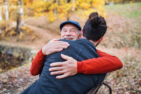Senior father and his young son sitting on bench by lake in nature, hugging. - HPIF26737