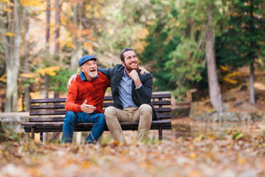 Älterer Vater und sein kleiner Sohn sitzen auf einer Bank am See in der Natur und unterhalten sich. - HPIF26741