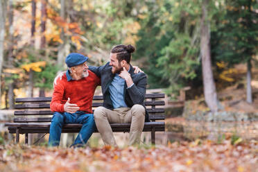 Senior father and his young son sitting on bench by lake in nature, talking. - HPIF26742