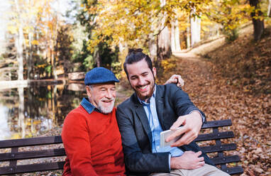 Senior father and his son with smartphone sitting on bench in nature, taking selfie. - HPIF26746