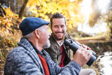 Senior father and his son with binoculars sitting on bench in nature, talking. - HPIF26751