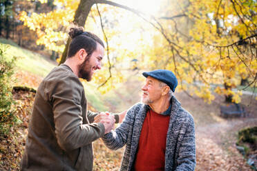 Ein älterer Vater und sein Sohn gehen in der Natur spazieren und schütteln sich beim Gespräch die Hände. - HPIF26758