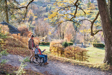 Ein älterer Vater mit Rollstuhl und sein Sohn auf einem Spaziergang in der Natur. - HPIF26760