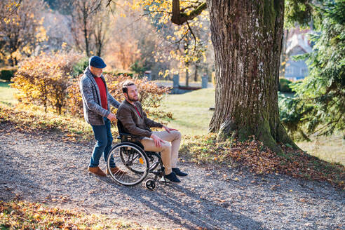 Ein älterer Vater mit Rollstuhl und sein Sohn auf einem Spaziergang in der Natur. - HPIF26761