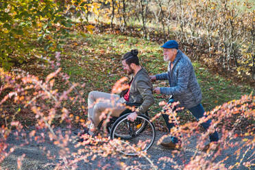 Ein älterer Vater und sein Sohn im Rollstuhl bei einem Spaziergang in der Natur. - HPIF26762