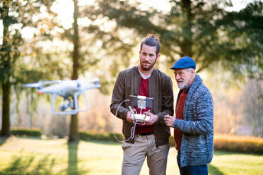 Älterer Vater und sein junger Sohn mit Drohne in der Natur, im Gespräch. - HPIF26765