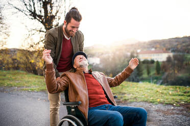 A young man and his senior father in wheelchair on a walk in town at sunset. - HPIF26780