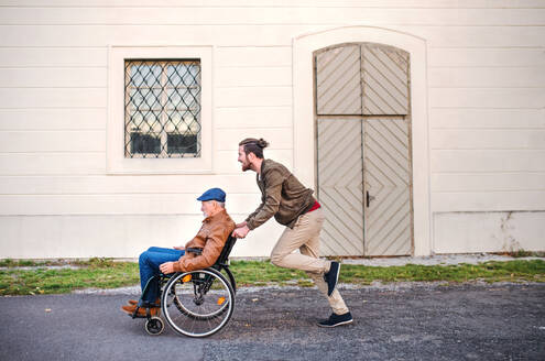 Ein junger Mann und sein älterer Vater im Rollstuhl machen einen Spaziergang durch die Stadt und haben Spaß. - HPIF26781