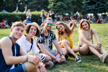 Eine Gruppe fröhlicher junger Freunde sitzt beim Sommerfest auf dem Boden und schaut in die Kamera. - HPIF26787