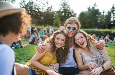 Eine Gruppe fröhlicher junger Freunde sitzt beim Sommerfest auf dem Boden und hat Spaß. - HPIF26791