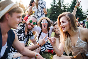 Group of cheerful young friends sitting on ground at summer festival, talking. - HPIF26794