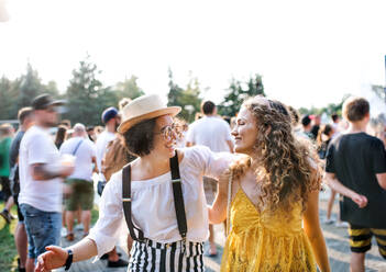 Zwei junge Freundinnen gehen Arm in Arm auf einem Sommerfest. - HPIF26808