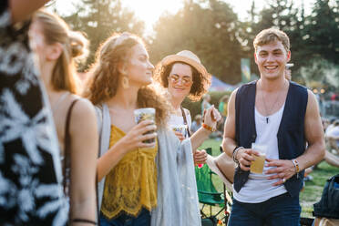 Eine Gruppe junger Freunde mit Getränken auf einem Sommerfest, die stehen und sich unterhalten. - HPIF26816
