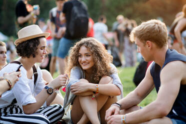 Eine Gruppe fröhlicher junger Freunde sitzt beim Sommerfest auf dem Boden und unterhält sich. - HPIF26832