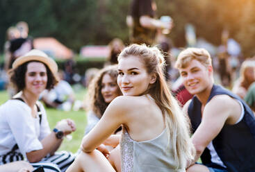 Eine Gruppe fröhlicher junger Freunde sitzt beim Sommerfest auf dem Boden und schaut in die Kamera. - HPIF26834