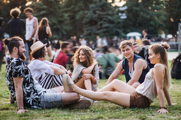 Eine Gruppe fröhlicher junger Freunde sitzt bei einem Sommerfest auf dem Boden. - HPIF26836