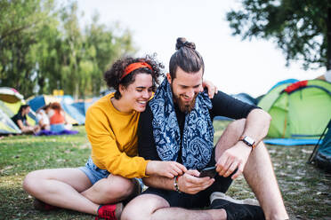 Ein junges Paar mit Smartphone beim Sommerfest, auf dem Boden sitzend. - HPIF26857