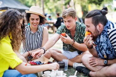 Eine Gruppe junger, fröhlicher Freunde beim Sommerfest, die auf dem Boden sitzen und essen. - HPIF26868