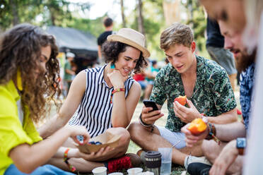 Eine Gruppe junger, fröhlicher Freunde beim Sommerfest, die auf dem Boden sitzen und essen. - HPIF26869