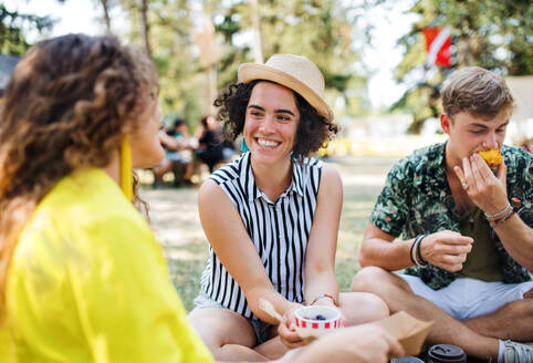 Eine Gruppe junger, fröhlicher Freunde beim Sommerfest, die auf dem Boden sitzen und essen. - HPIF26870