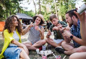 Eine Gruppe junger, fröhlicher Freunde beim Sommerfest, die auf dem Boden sitzen und essen. - HPIF26871