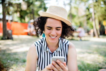 Front view of young woman at summer festival or camping holiday, using smartphone. - HPIF26873