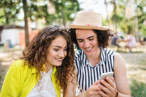 Ein Porträt von zwei jungen Freundinnen auf einem Sommerfest, die ein Smartphone benutzen. - HPIF26874
