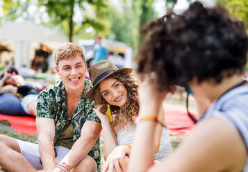 Group of cheerful young friends sitting on ground at summer festival, talking. - HPIF26892