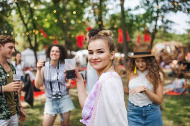 Eine Gruppe junger Freunde mit Getränken auf einem Sommerfest, die stehen und sich unterhalten. - HPIF26903