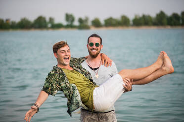 Cheerful young men friends having fun at summer festival, standing in lake. - HPIF26946