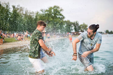 Fröhliche junge Männer, die sich auf einem Sommerfest amüsieren, stehen im See. - HPIF26956
