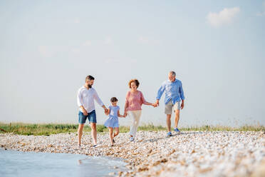 Eine Mehrgenerationenfamilie, die im Urlaub am See spazieren geht und sich an den Händen hält. - HPIF26980