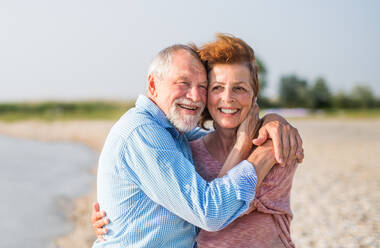 Front view of senior couple on a holiday on a walk by the lake, hugging. - HPIF26982