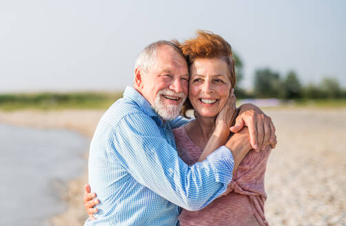 Vorderansicht eines älteren Paares im Urlaub bei einem Spaziergang am See, das sich umarmt. - HPIF26982