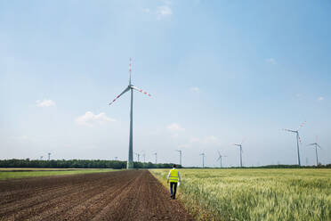 Rückansicht eines Ingenieurs, der auf einem Feld in einem Windpark spazieren geht, Kopierraum. - HPIF26987