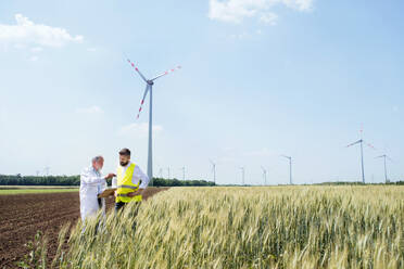 Zwei Ingenieure oder Techniker mit Klemmbrett stehen im Windpark und machen sich Notizen. - HPIF26989