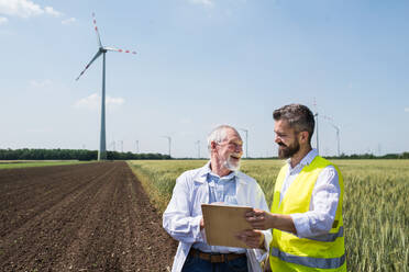 Zwei Ingenieure oder Techniker mit Klemmbrett stehen im Windpark und machen sich Notizen. - HPIF26990