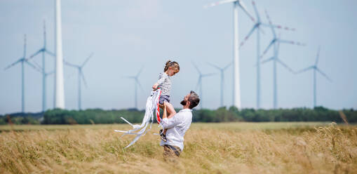 Reifer Vater mit kleiner Tochter steht auf einem Feld in einem Windpark und spielt. - HPIF26999