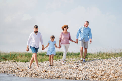Eine Mehrgenerationenfamilie, die im Urlaub am See spazieren geht und sich an den Händen hält. - HPIF27011