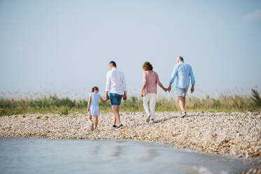 Rückansicht einer Mehrgenerationen-Familie im Urlaub bei einem Spaziergang am See, beim Laufen. - HPIF27012