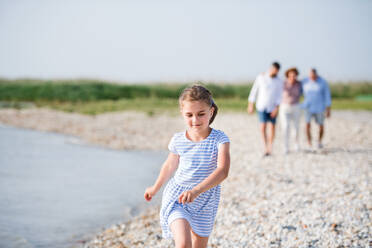 Ein kleines Mädchen, das mit seiner Familie im Urlaub am See spazieren geht und sich an den Händen hält. - HPIF27014