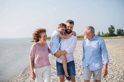 Eine Mehrgenerationenfamilie, die im Urlaub am See spazieren geht und sich an den Händen hält. - HPIF27017