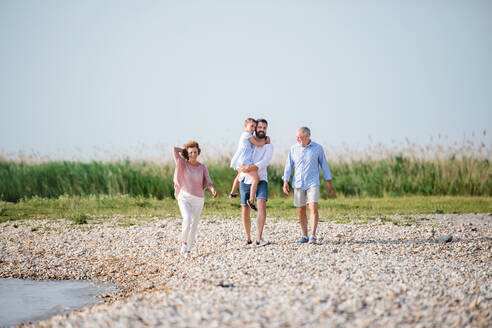 Eine Mehrgenerationenfamilie, die im Urlaub am See spazieren geht und sich an den Händen hält. - HPIF27018