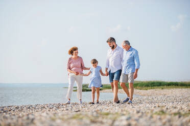 Eine Mehrgenerationenfamilie, die im Urlaub am See spazieren geht und sich an den Händen hält. - HPIF27019