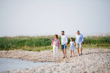 Eine Mehrgenerationenfamilie, die im Urlaub am See spazieren geht und sich an den Händen hält. - HPIF27021