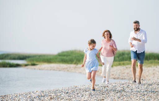 Eine Mehrgenerationenfamilie im Urlaub, die am See spazieren geht und läuft. - HPIF27023