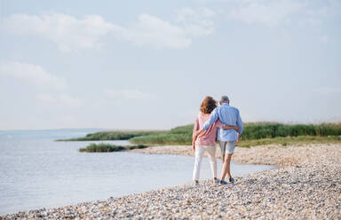 Rückansicht eines älteren Paares im Urlaub bei einem Spaziergang am See, das Arm in Arm geht. - HPIF27024